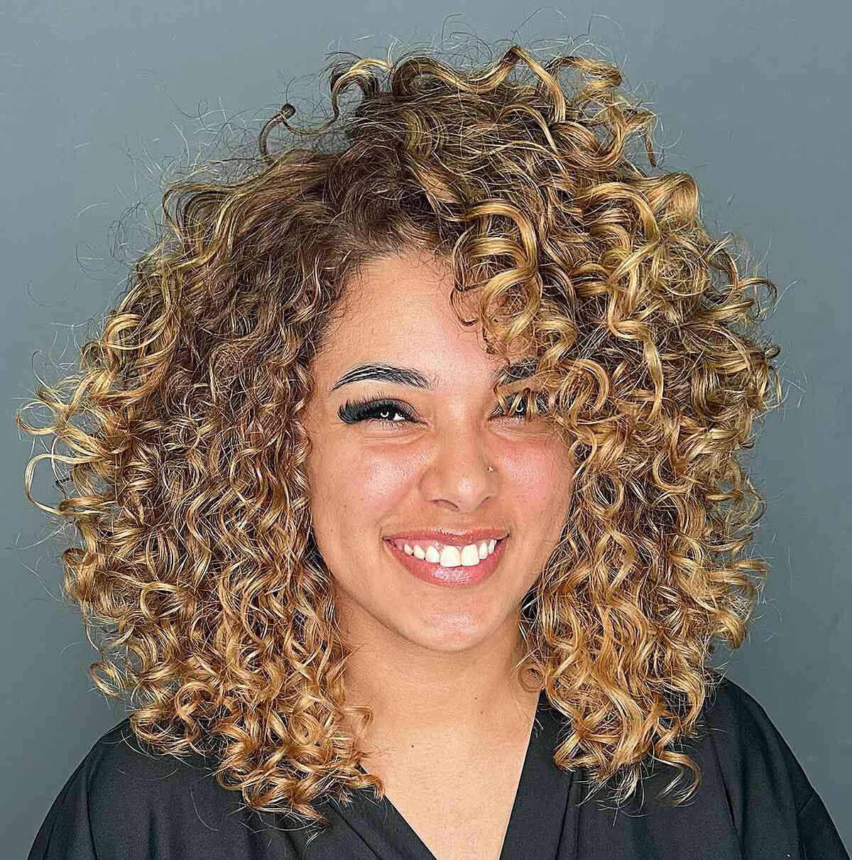 A woman with a Cadō cut featuring blonde curly hair and cascading layers that highlight the curls and create a voluminous style.
