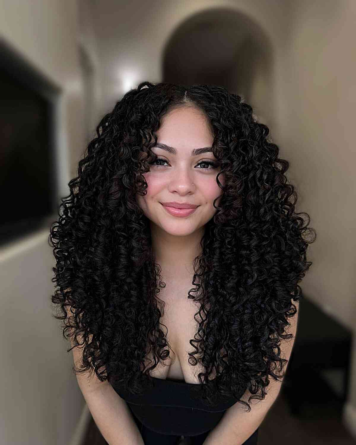 A woman with a Cadō cut that features long layers and defined curls, creating a glamorous yet practical style for natural curls.