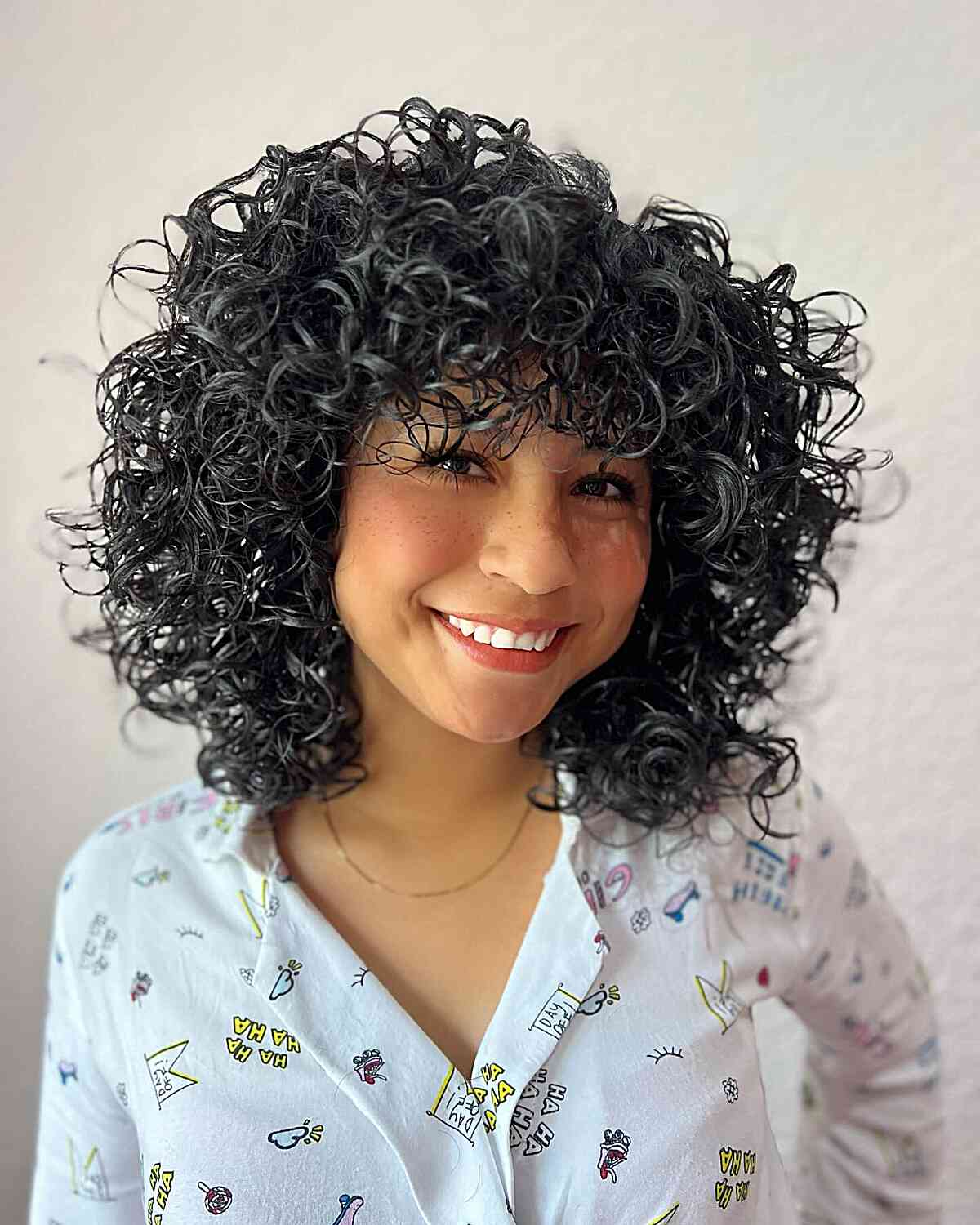 A woman with a curly textured Cadō cut with playful bangs, showcasing a soft face-framing effect and natural volume.