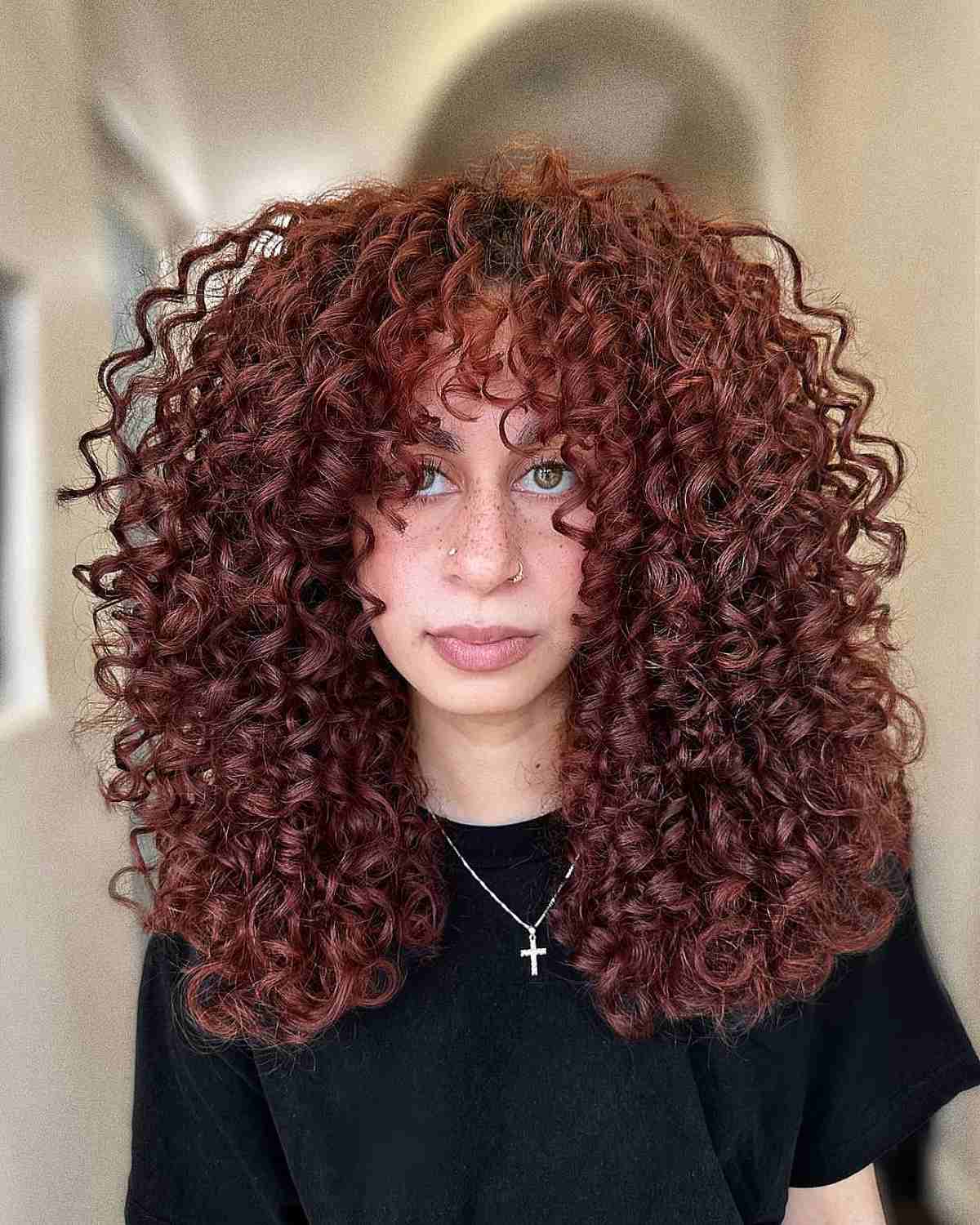 A woman with a face-framing Cadō cut accentuating thick curls in a rich auburn shade, ideal for enhancing natural volume.