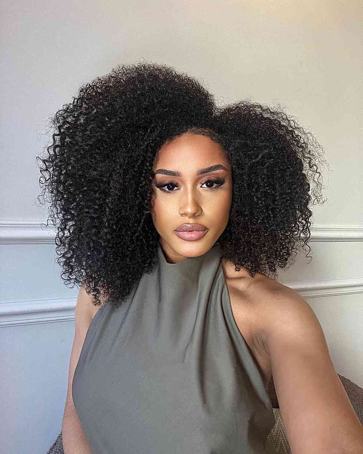 A woman with a side-parted medium afro Cadō cut, embracing the hair's natural volume and texture with an asymmetrical touch.