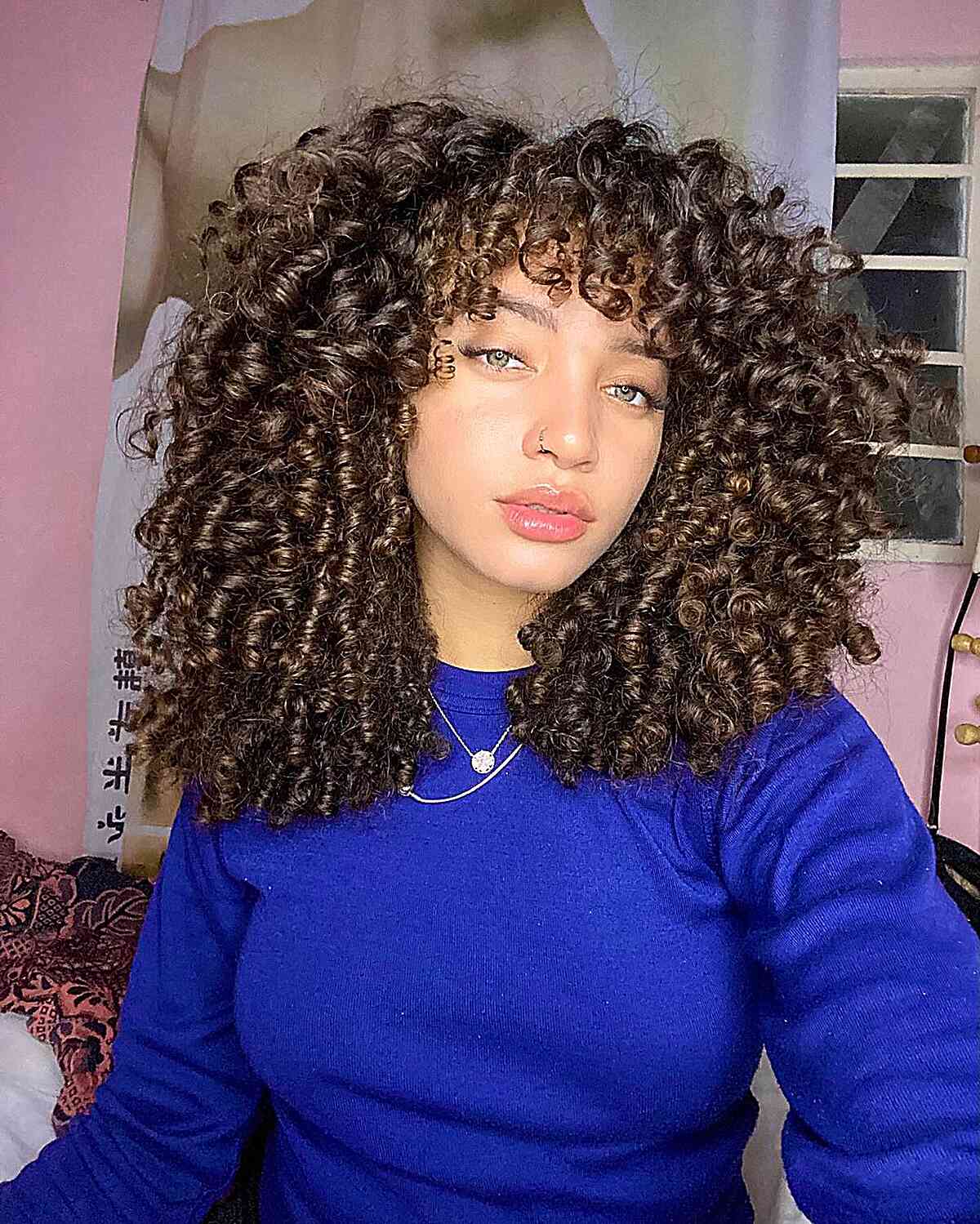 A woman with layered medium hair featuring springy curls, a Cadō cut that balances length and manageability while highlighting natural curl elasticity.
