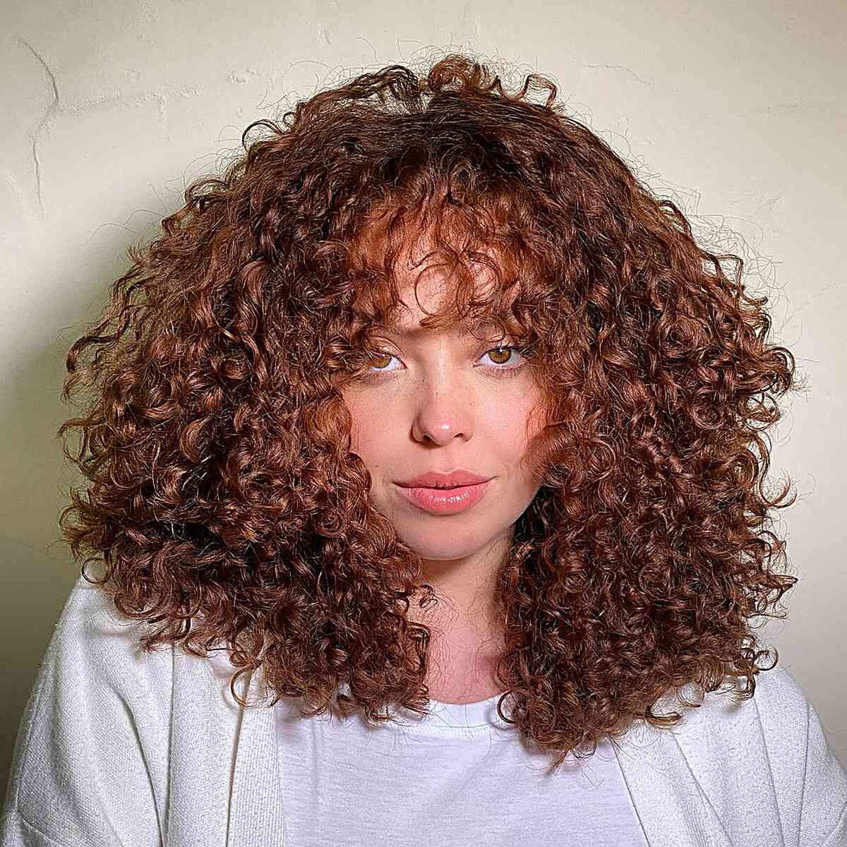 A woman with mid-length red curly hair with voluminous layers, expertly cut to enhance natural curls and reduce bulk.