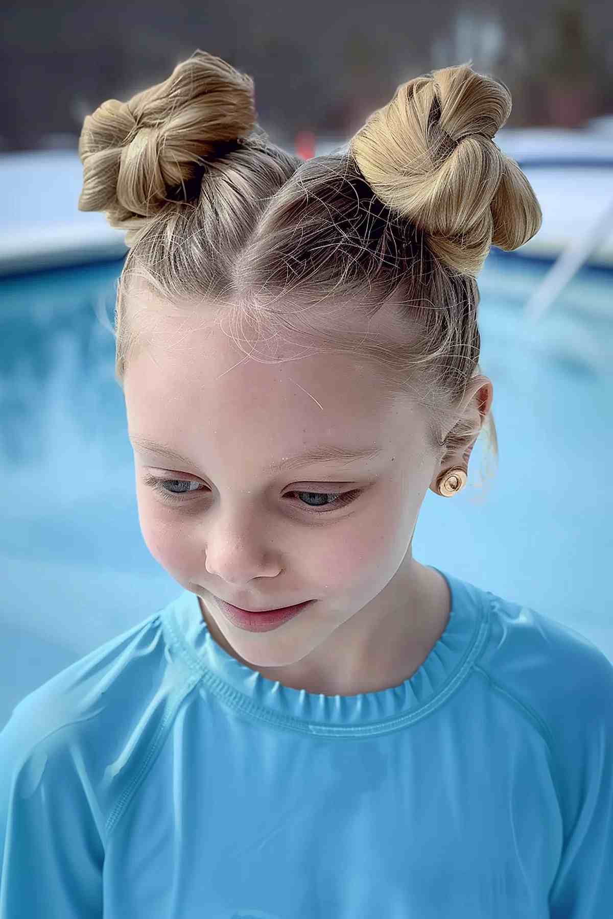 Girl with double buns, wearing a blue swimsuit by the pool