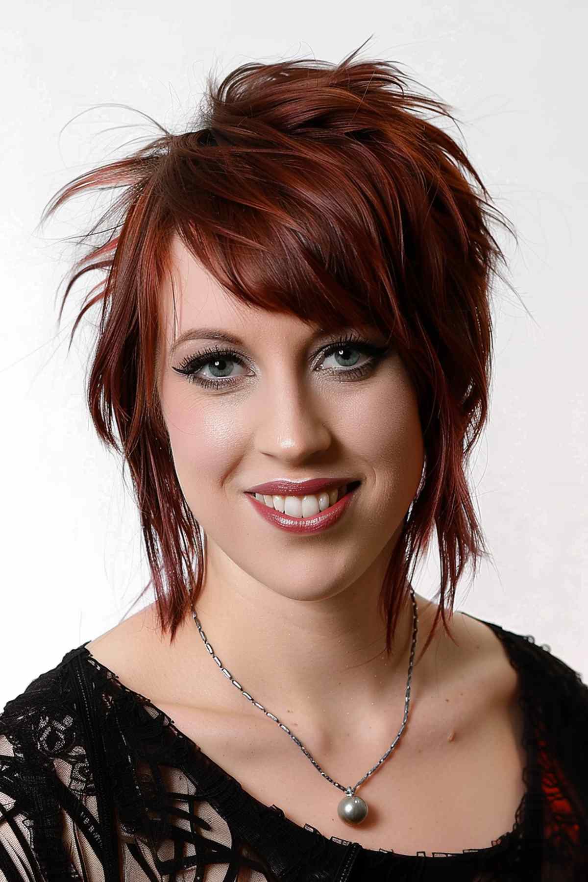 Woman with vibrant red hair featuring choppy layers and asymmetric bangs, designed to enhance volume and add a playful, modern twist.