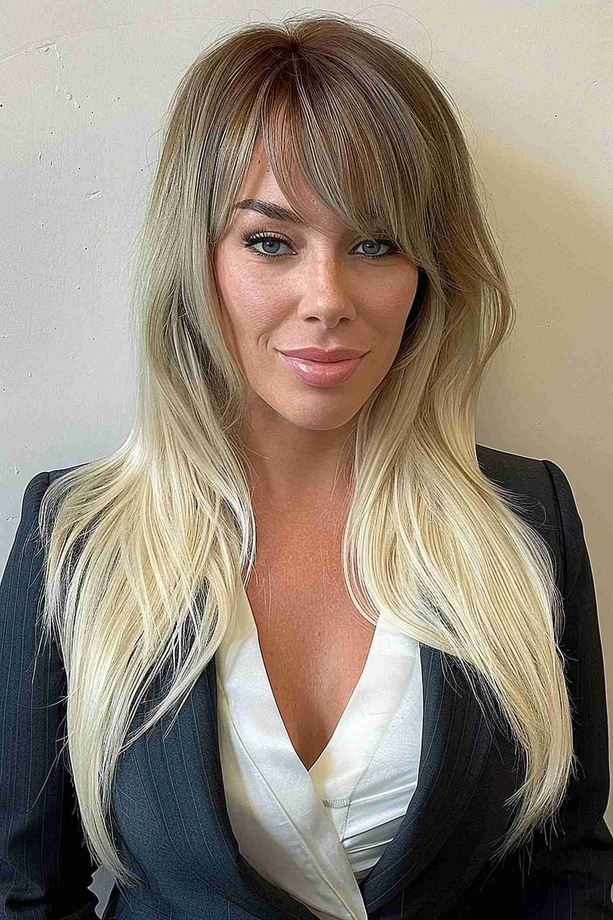 Woman with luxurious long blonde hair featuring an asymmetric fringe, enhancing volume and providing a flattering frame for the face.