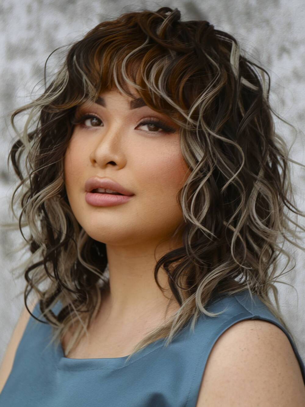 A wavy curly hairstyle with soft bangs, adding definition while complementing round face shapes beautifully