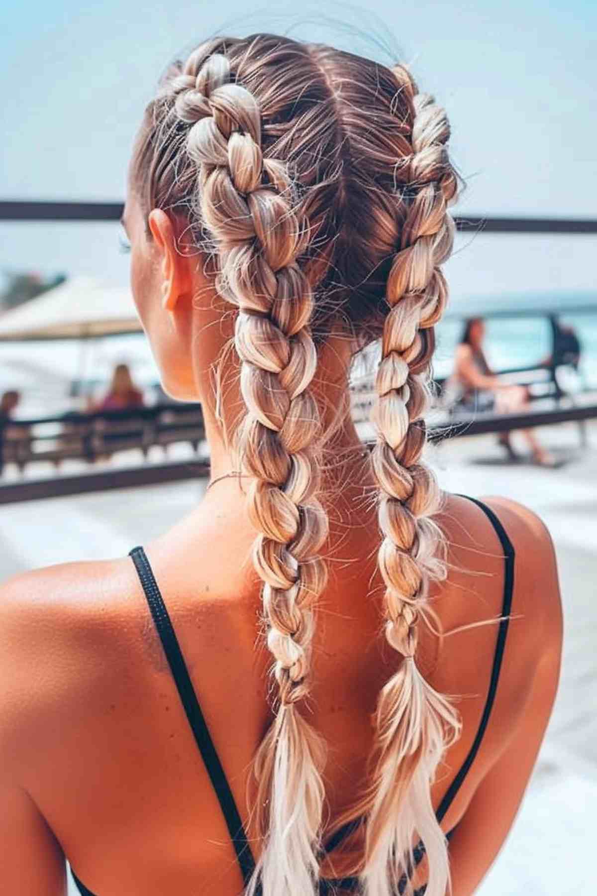 Woman with blonde Dutch braids at the beach, wearing a black swimsuit