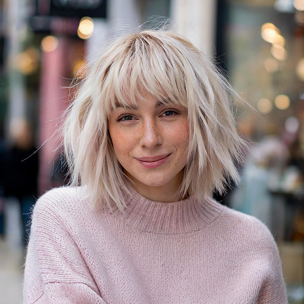 Choppy blonde bob with short curtain bangs, styled with messy waves for a modern, textured look