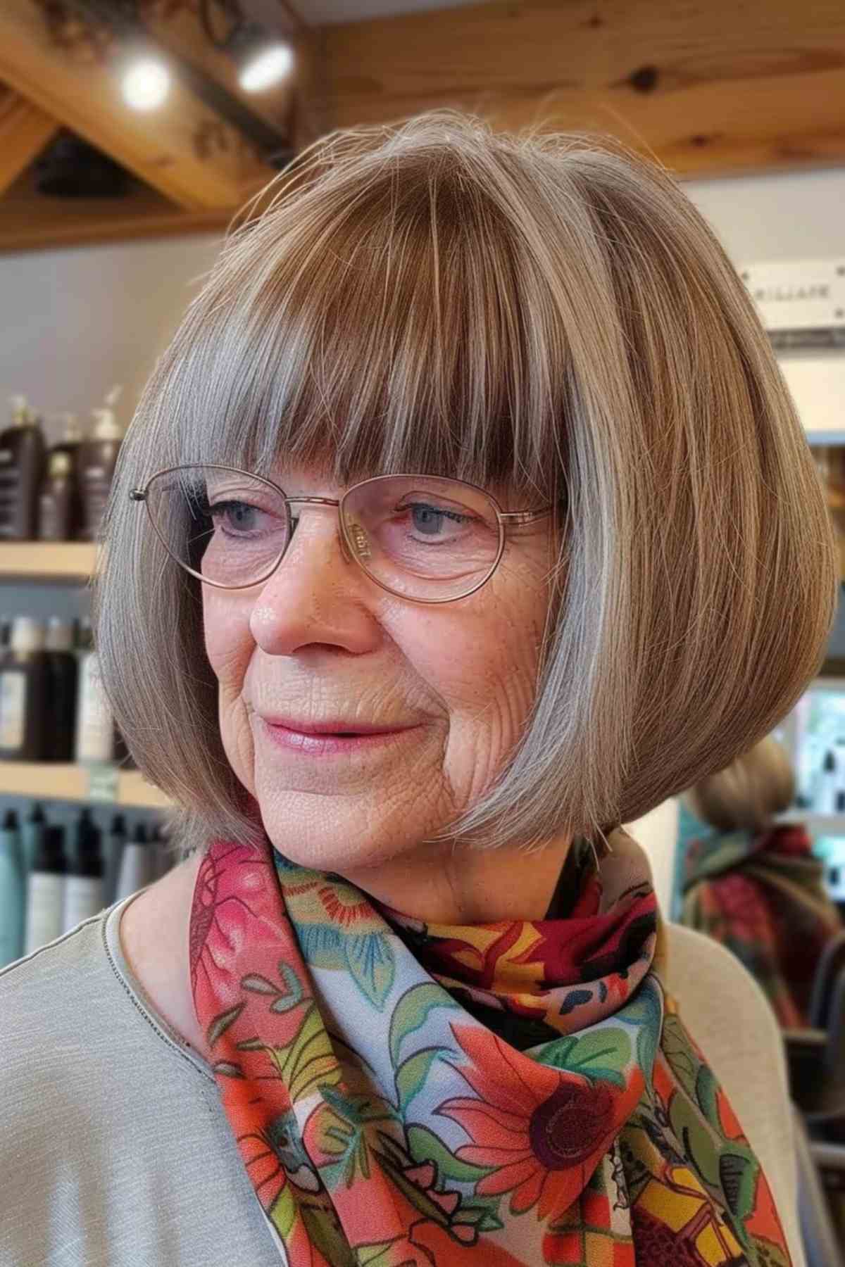 Mature woman with a classic bob haircut featuring full, straight bangs, wearing glasses and a floral scarf.