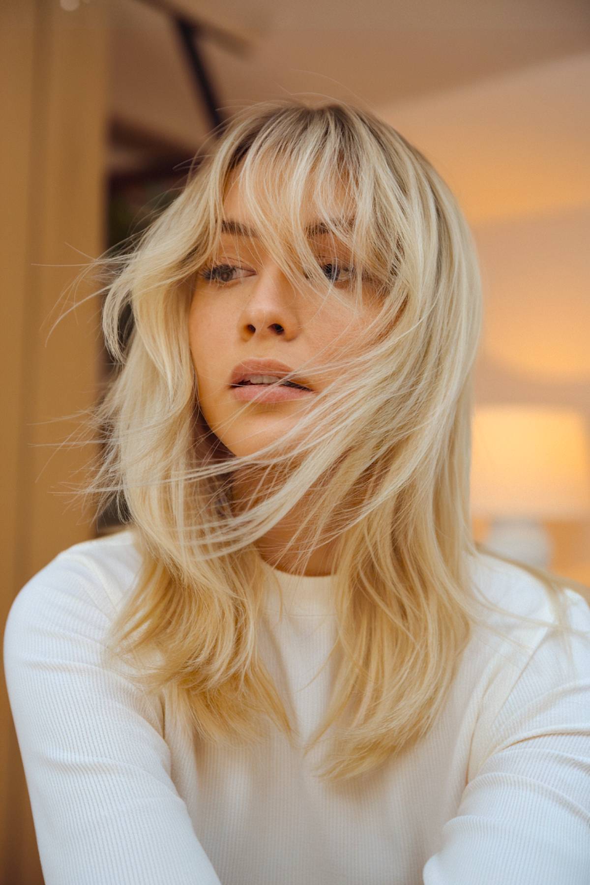 Soft, buttery blonde layers with ultra-light, wispy bangs for a delicate and airy effect