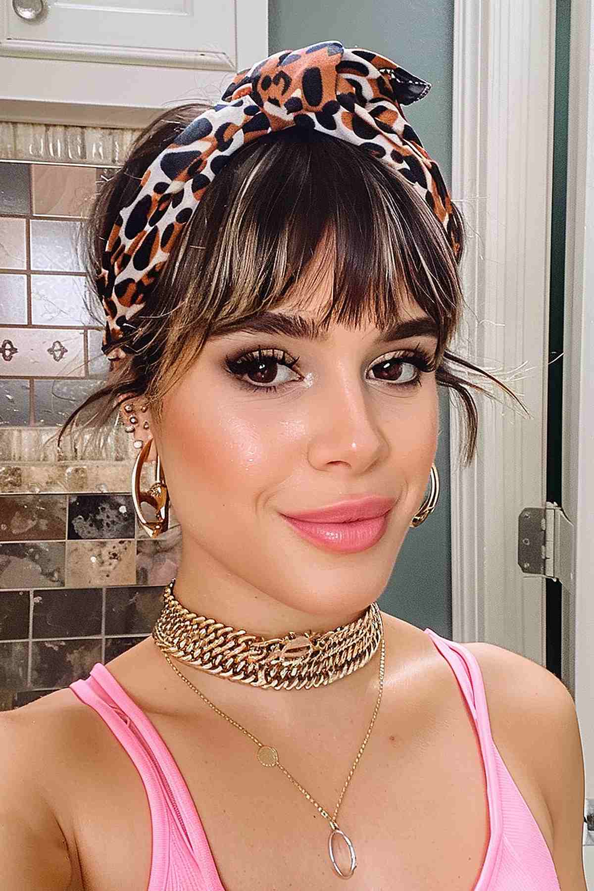 Woman with bangs and a chic headband, wearing gold jewelry and a pink top