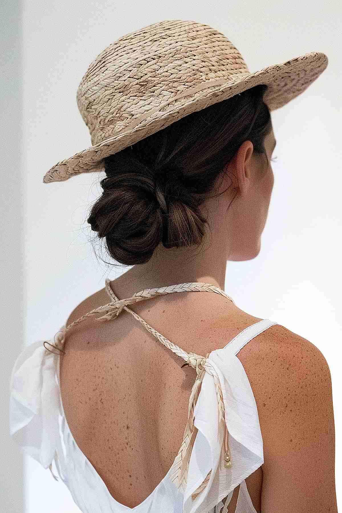 Woman with medium length hair in a chic low bun, wearing a hat and white top