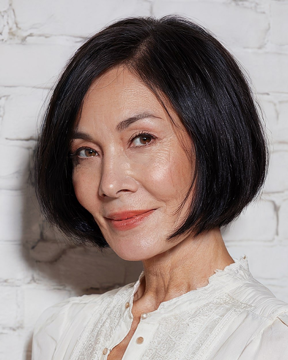 Chin-length bob with deep side part on sleek black hair for older women