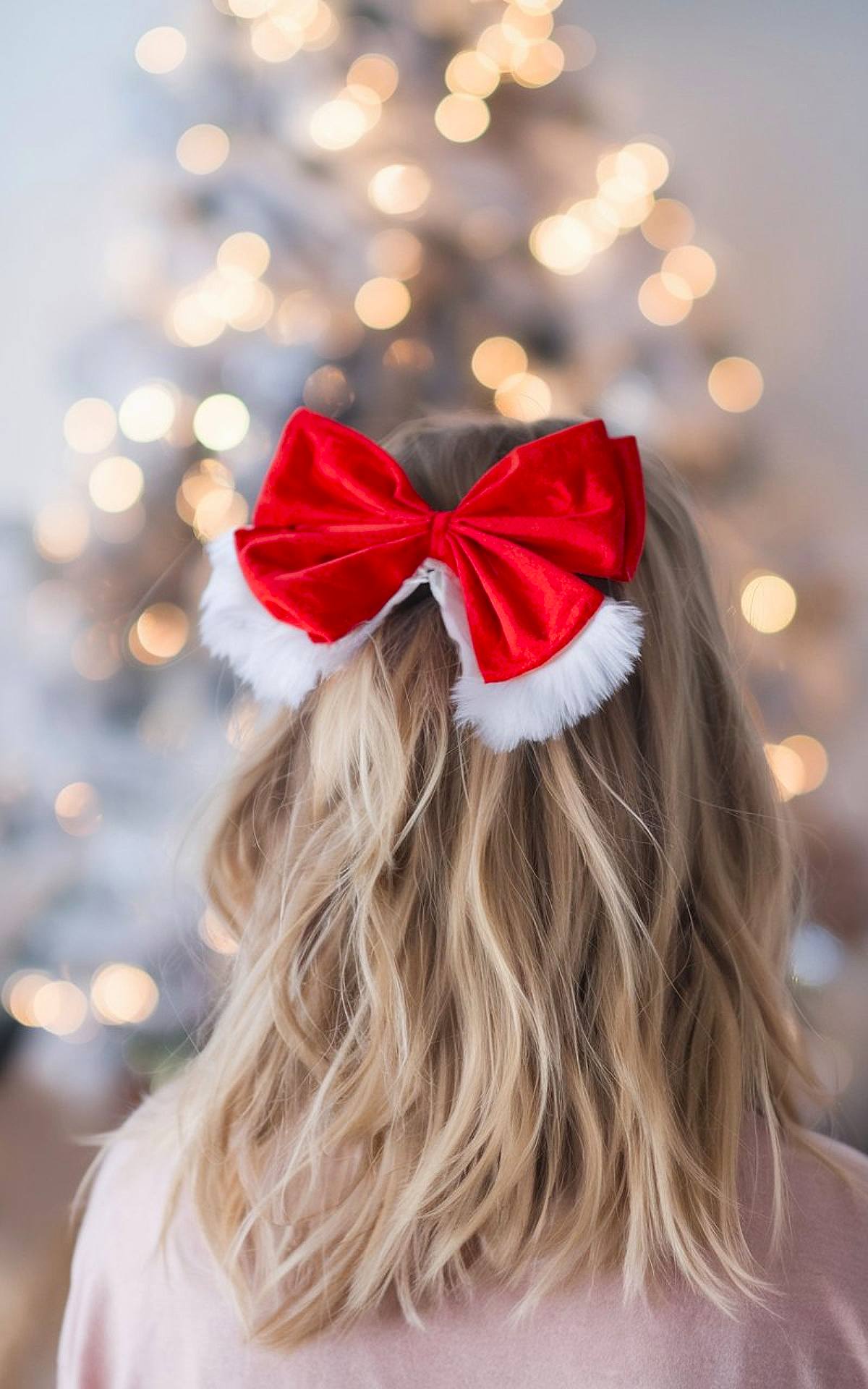 Half-up wavy hair with a red velvet and white faux fur bow for a festive Christmas hairstyle