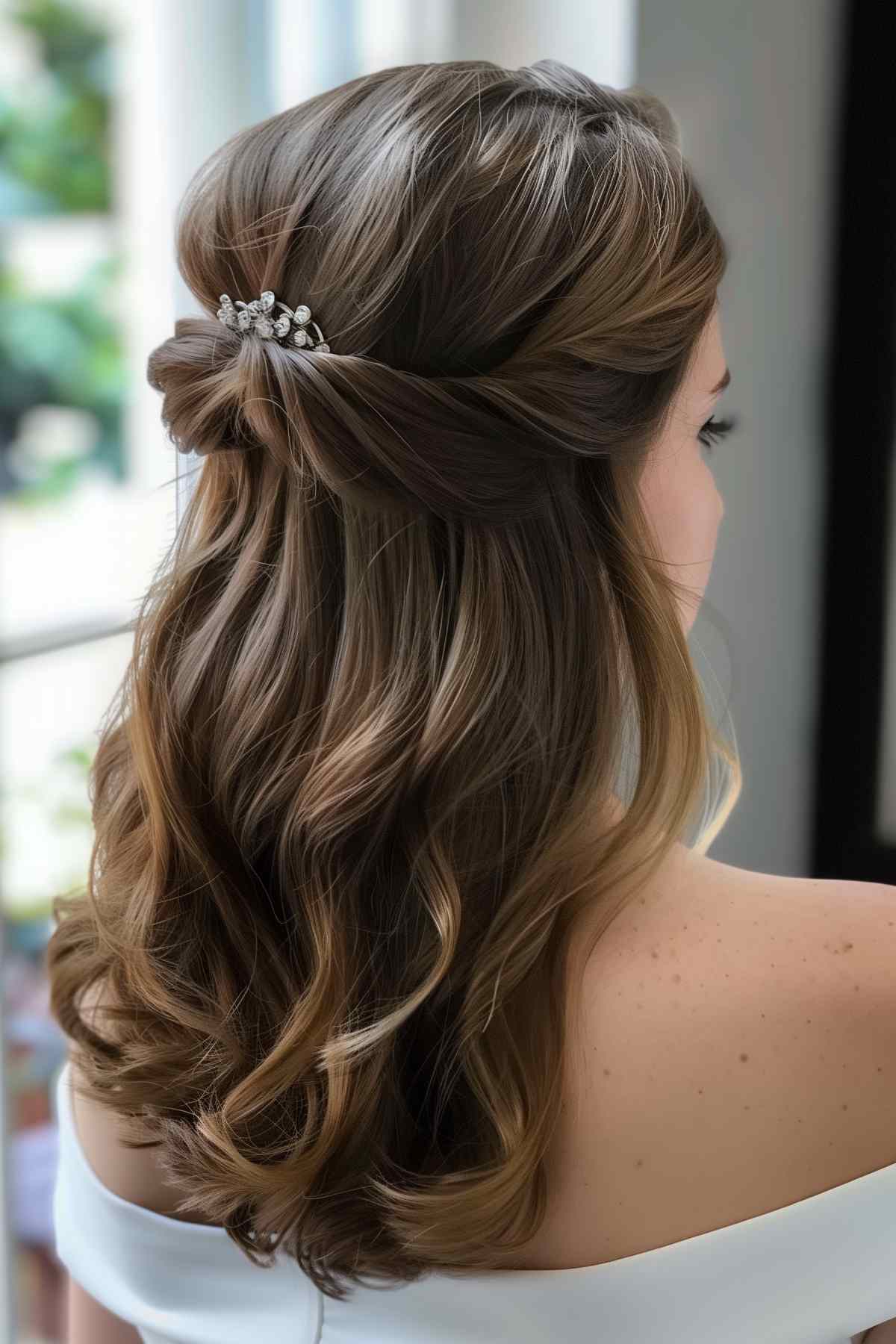 Bridal hairstyle with elegant half-up twist and crystal hair accessory in medium-length brown hair