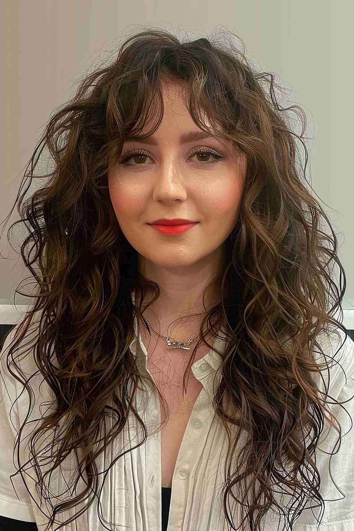 Woman with curly long layers and face-framing bangs, styled to enhance natural curls.