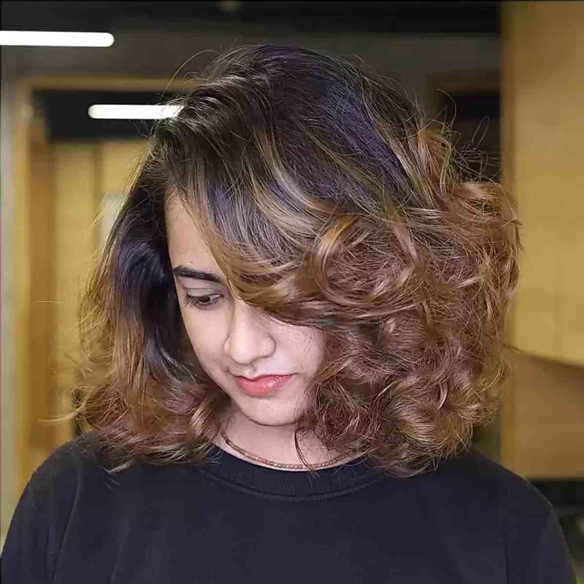 Dark-Rooted Curly Hair with Golden Brown Highlights on Shoulder-Length Cut with a Side Part