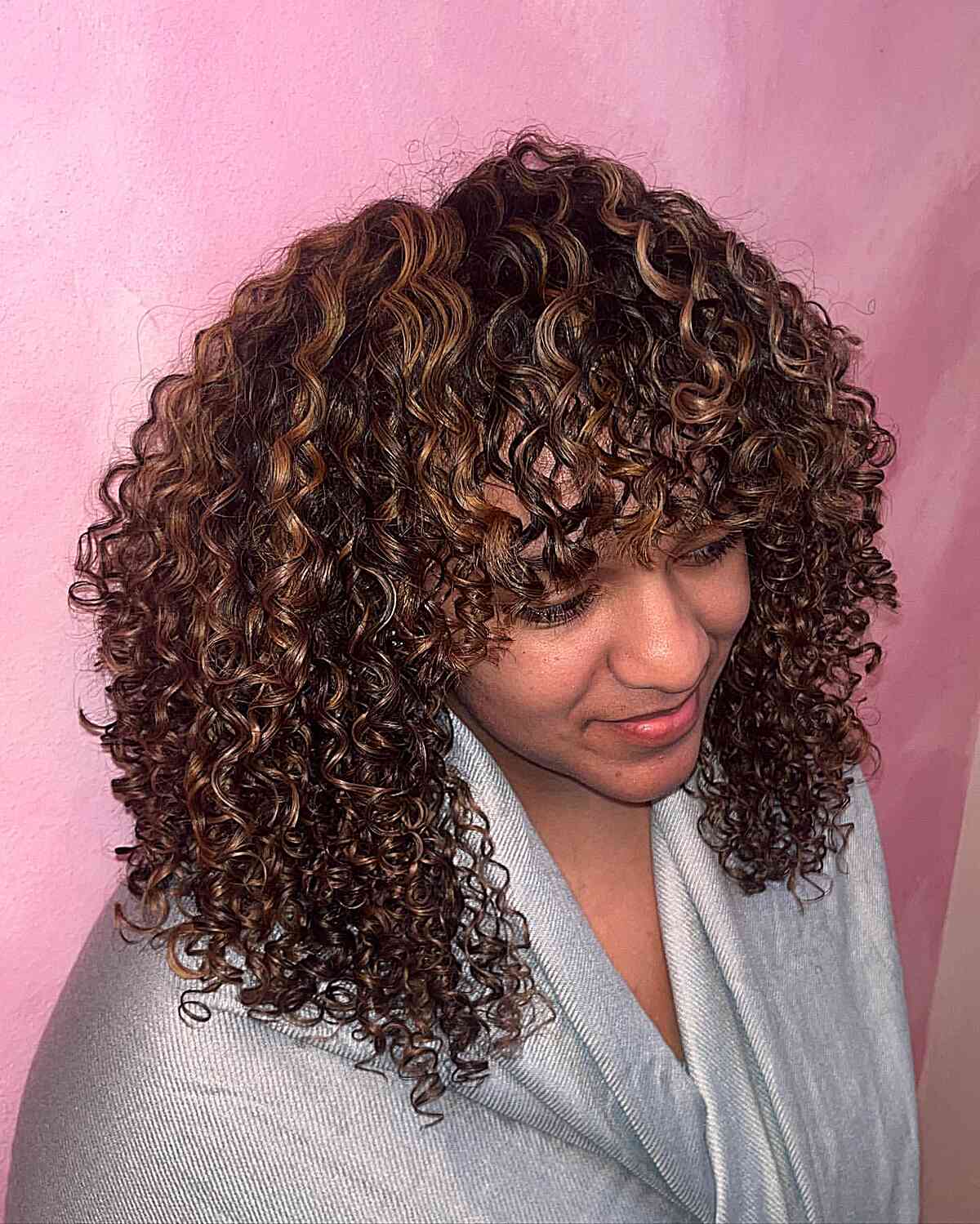 Dimensional Curly Caramel Hair Highlights for a Medium Layered Haircut with Bangs