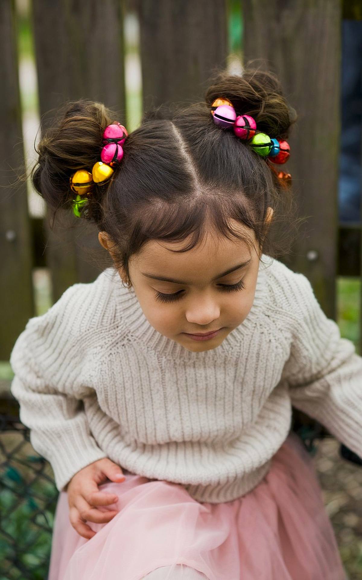 Child's hair in double buns with colorful jingle bell accessories for a Christmas look