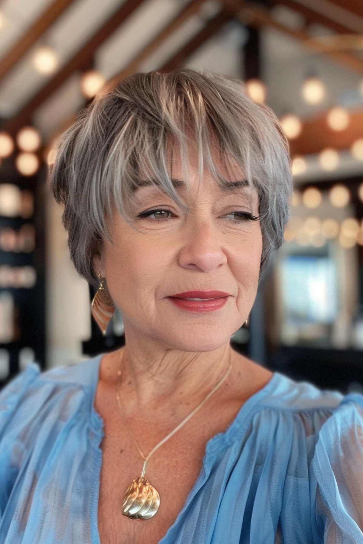 Mature woman with short, layered grey hair and easy wash-and-wear bangs, wearing a light blue blouse.