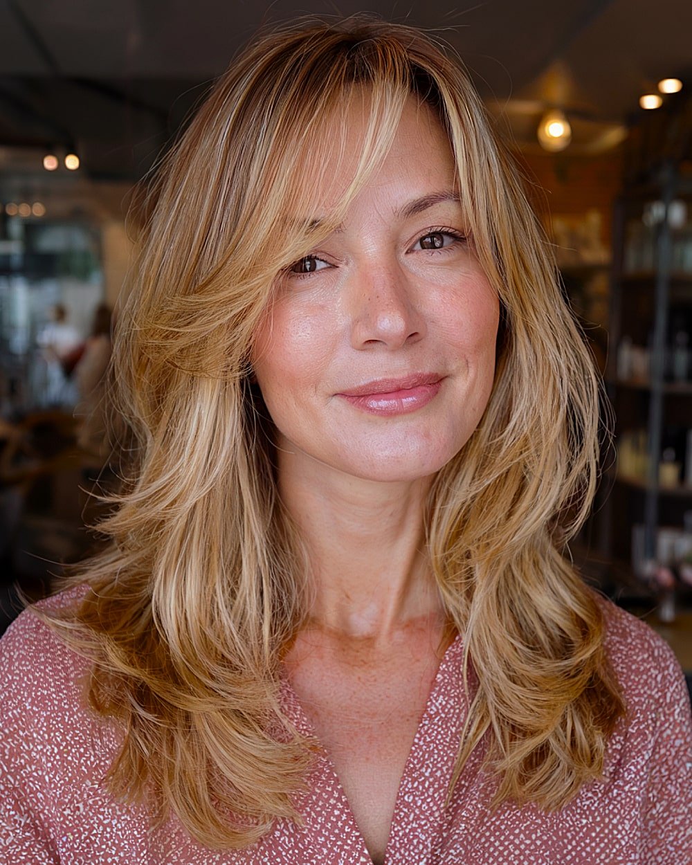 Long golden blonde layers with side-swept bangs and soft fall waves for a classic seasonal hairstyle