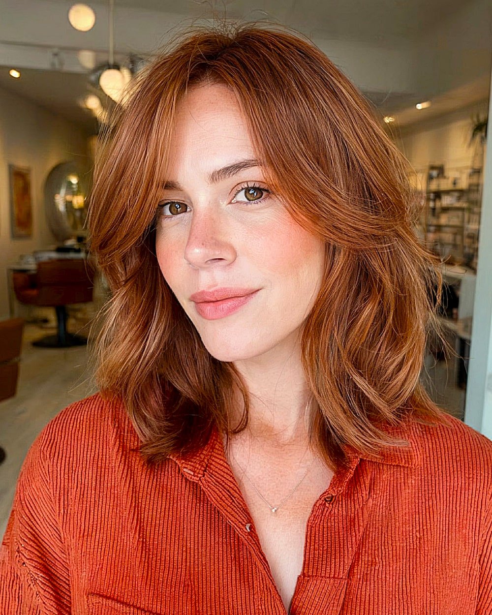 Pumpkin spice layered lob with soft face-framing waves and warm copper-red color for fall hair inspiration