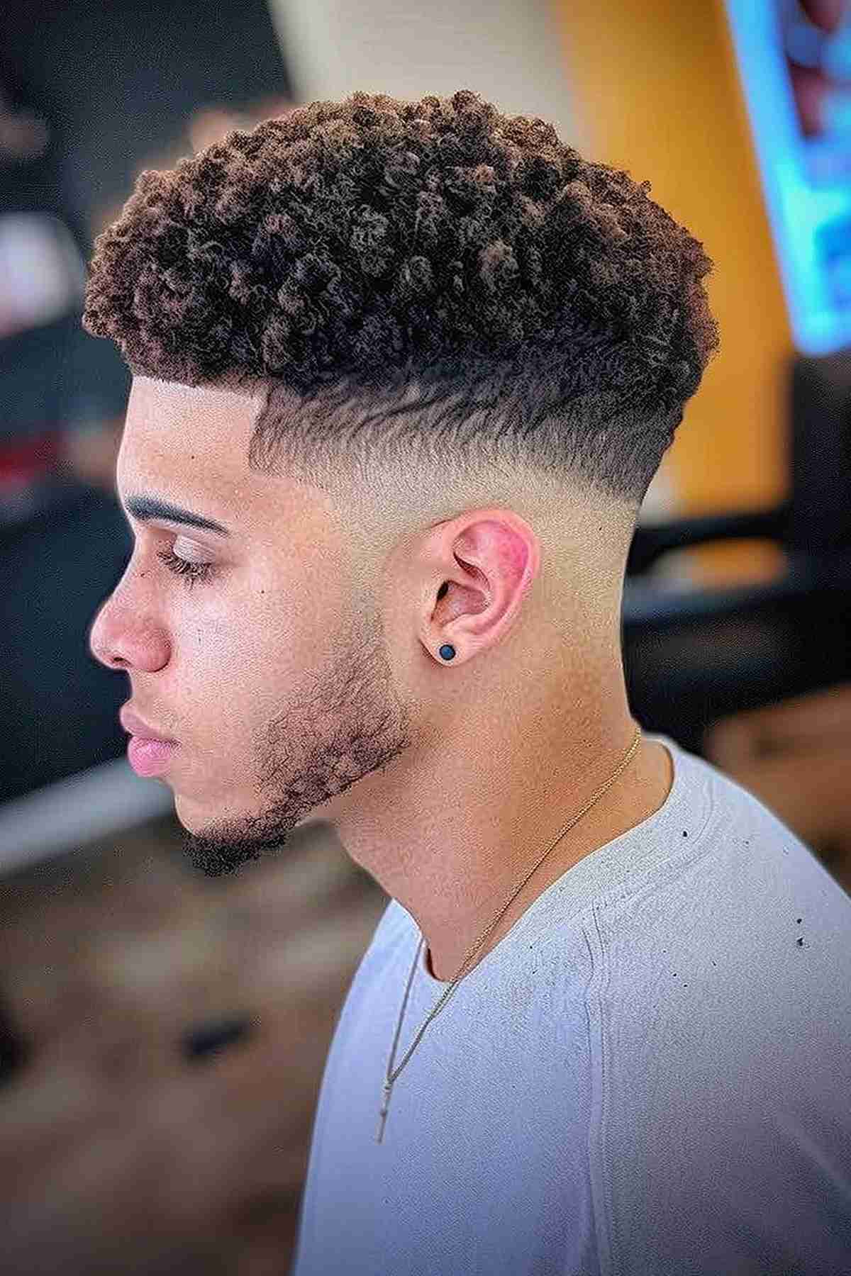 Low bald fade with natural curly hair on top, showcasing sharp, clean lines around the ears and temple.
