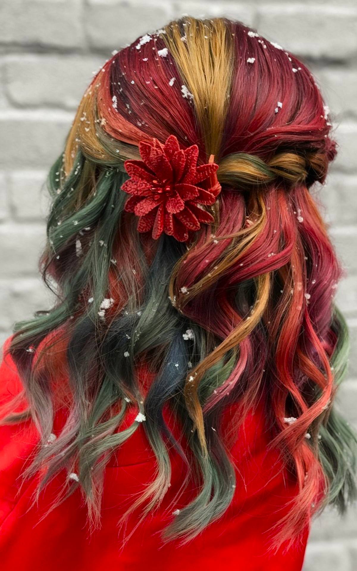 Half-up hairstyle with red, green, and gold waves and a poinsettia clip for a festive Christmas look