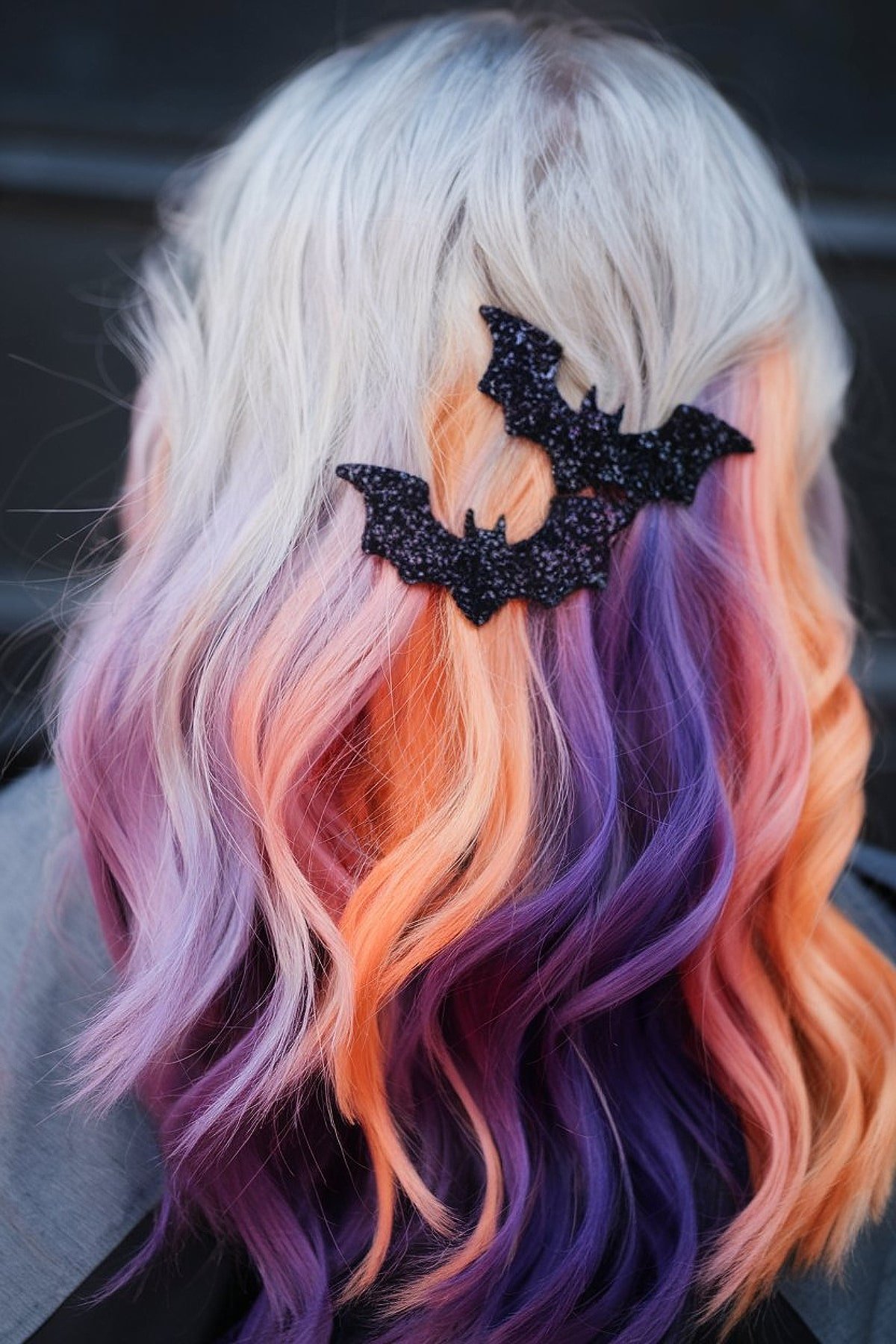 Pastel lilac, peach, and purple hair styled in waves with glittery bat clips for Halloween