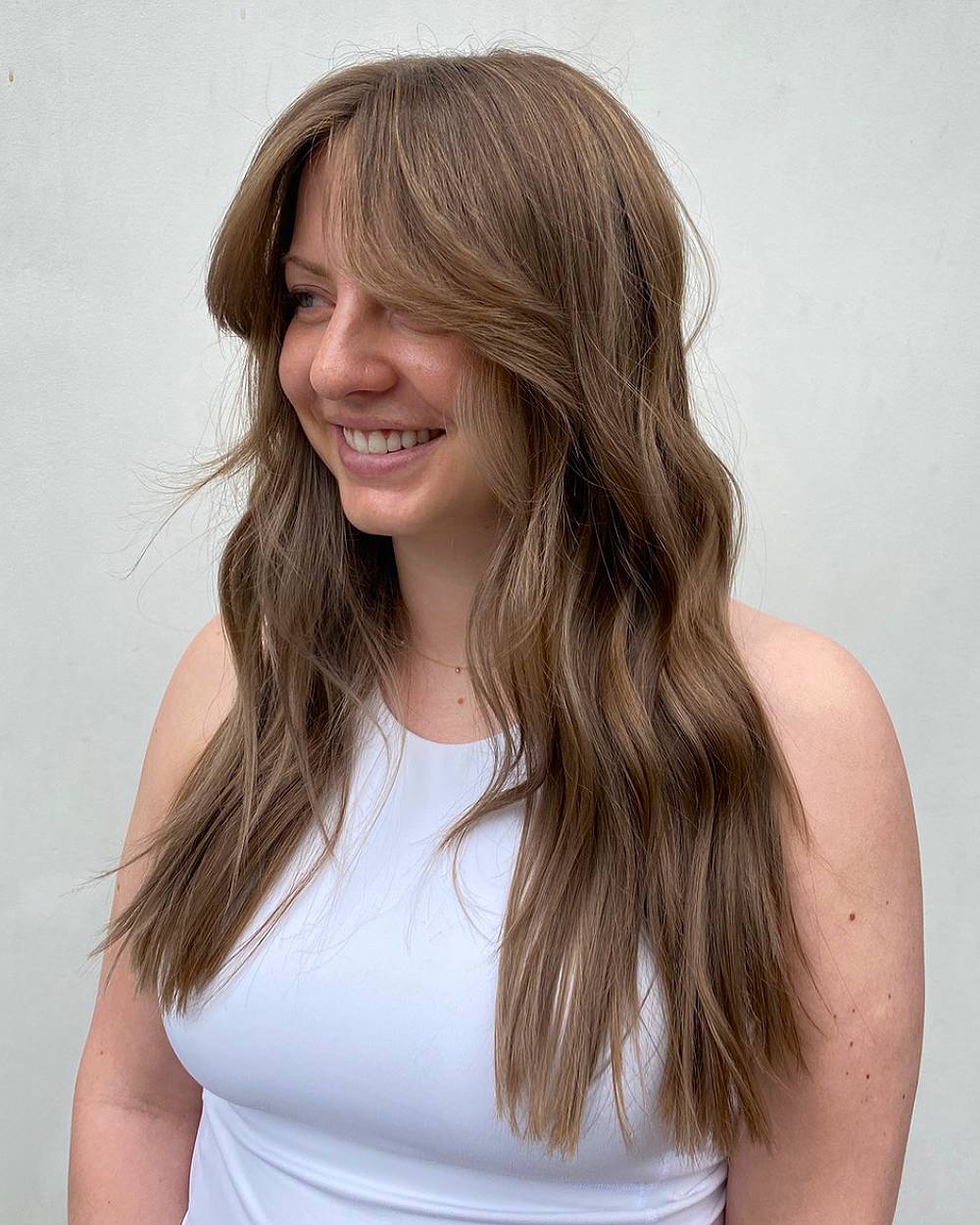 Cabello castaño claro suave con capas y flequillo que enmarca el rostro