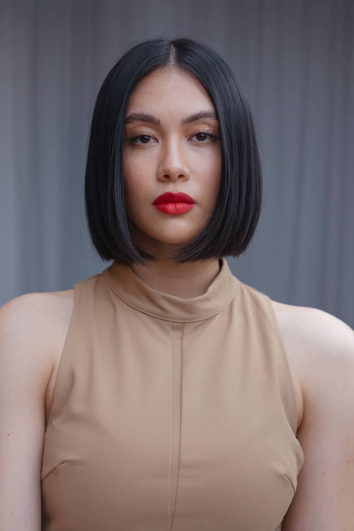 Sleek, jaw-length blunt bob with a middle part, paired with a glossy, jet-black finish for a chic glam look