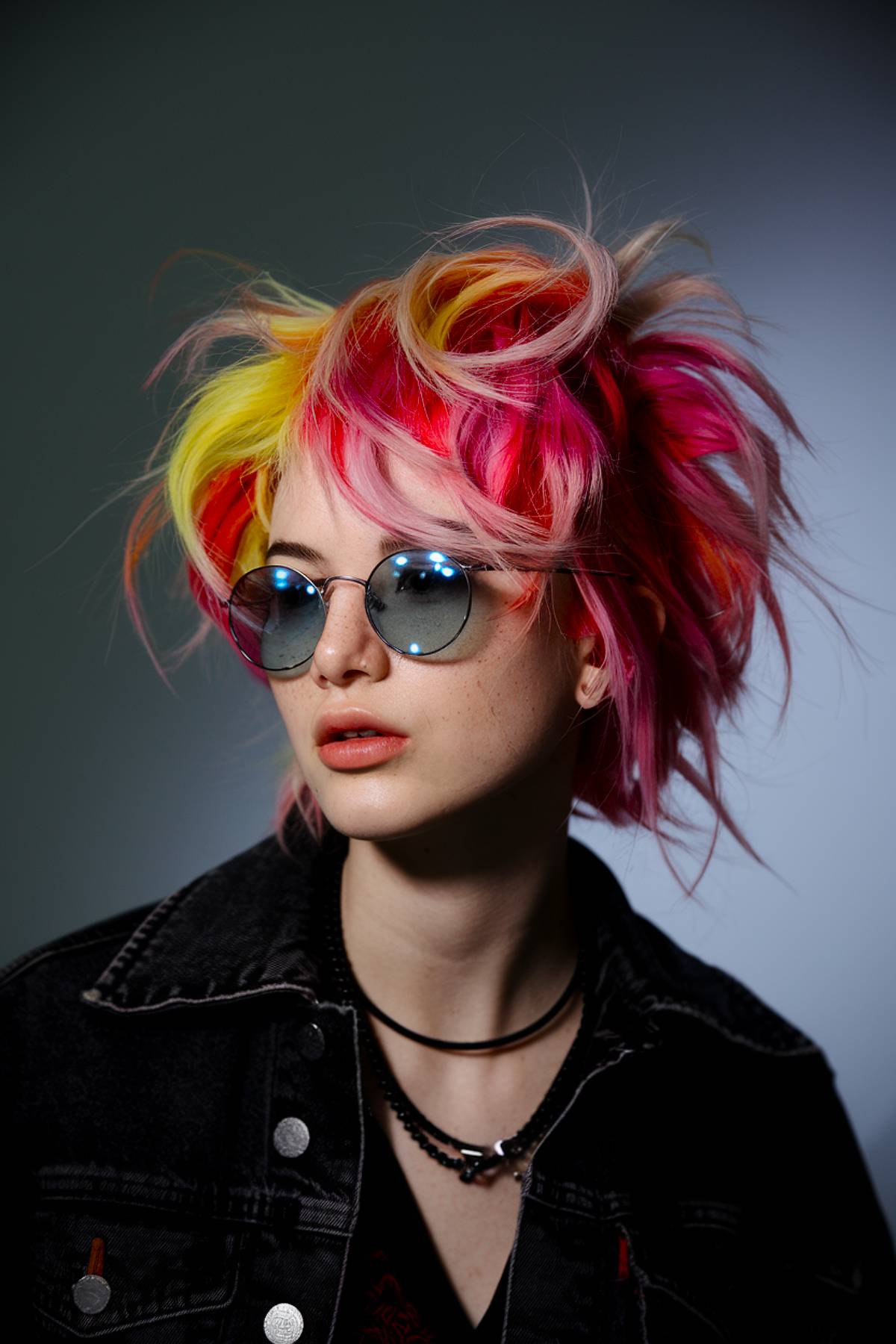 Edgy, choppy short hairstyle with neon pink, yellow, and red hues, creating a bold glam rock statement