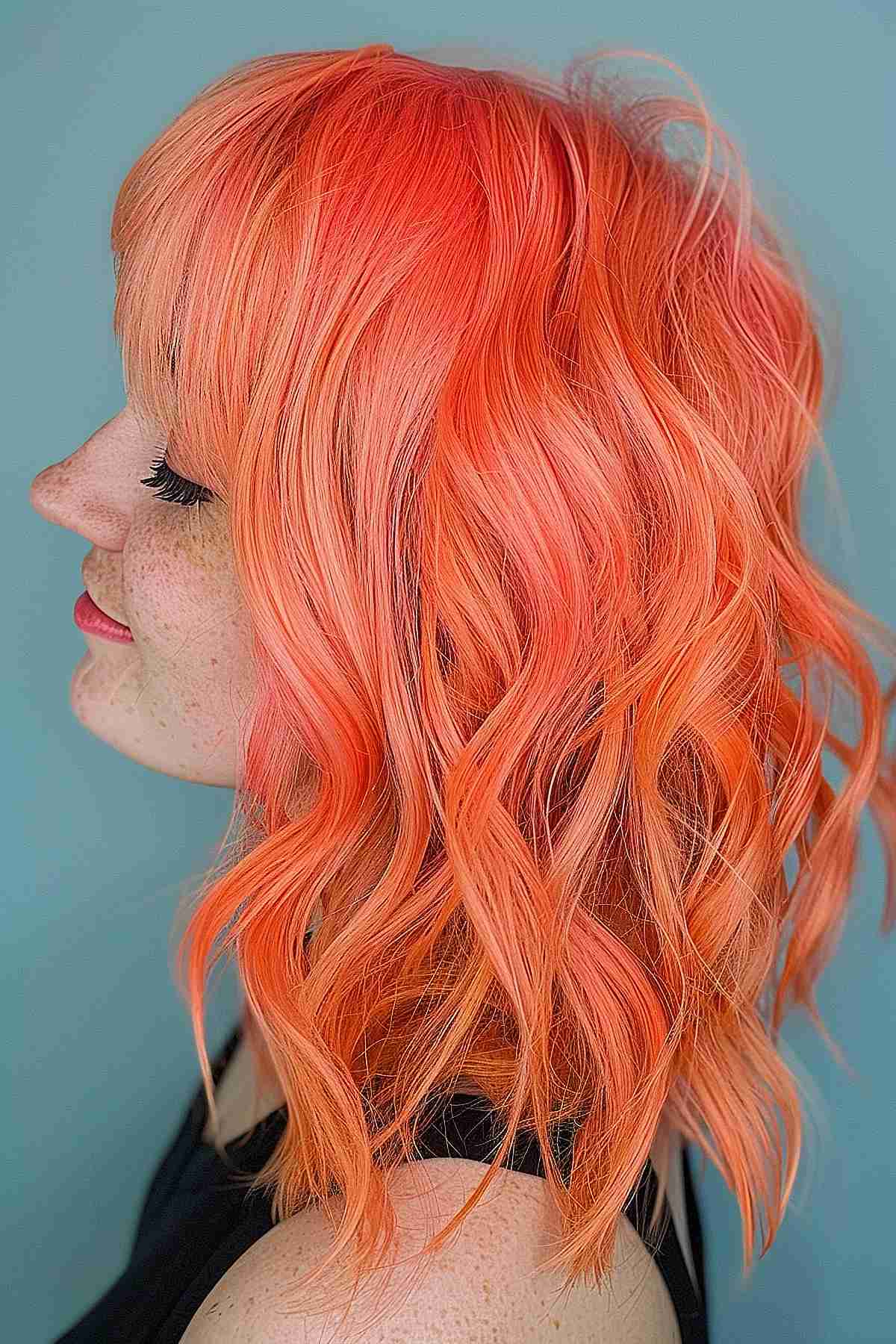 Vibrant electric peach hair styled into soft waves, offering a bold and energetic burst of color that enhances volume and texture.