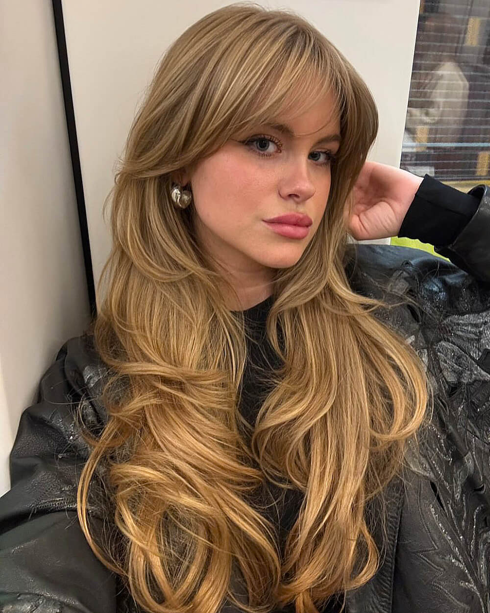 Honey blonde blowout with long curtain bangs and layered ends for thick, voluminous hair