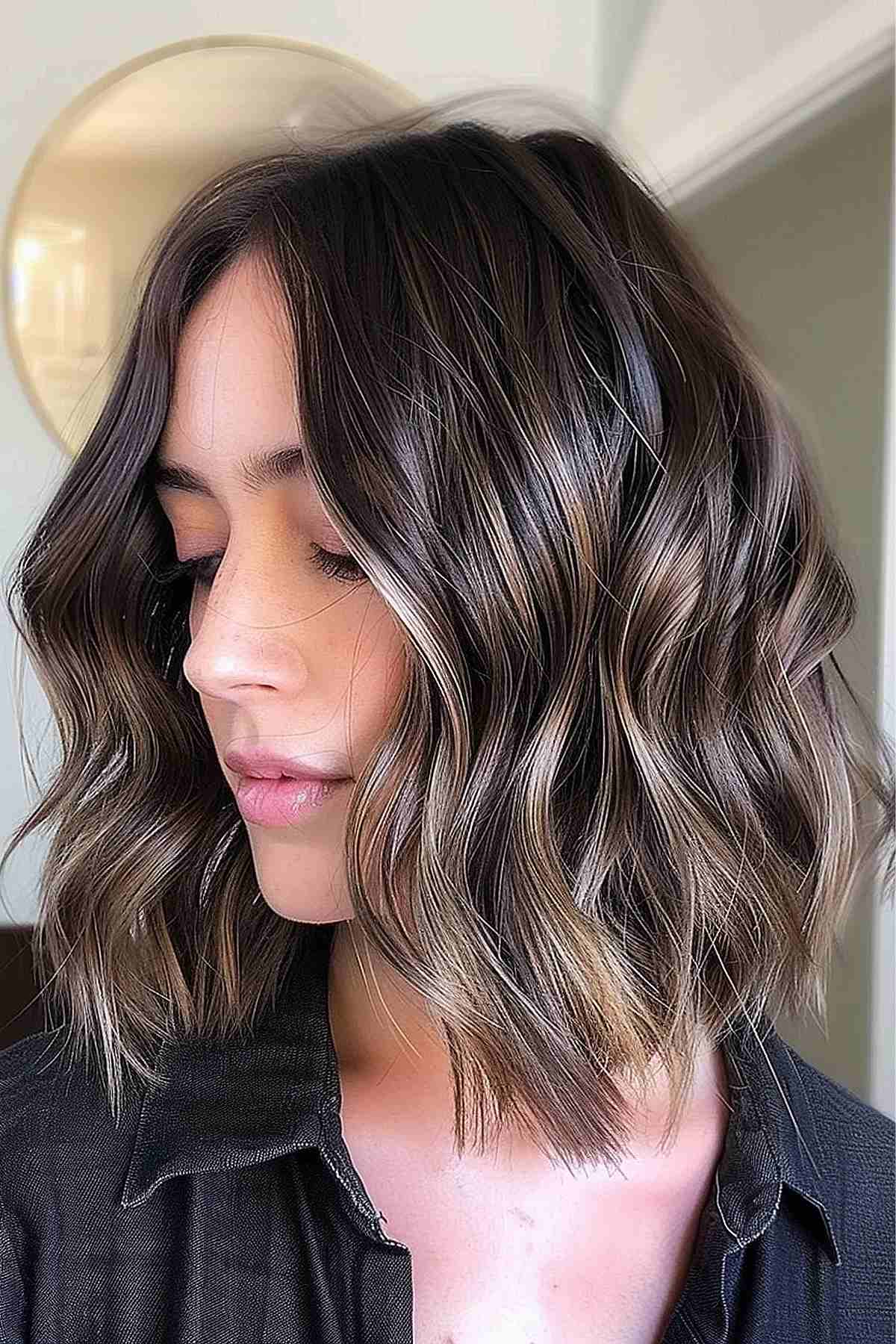 Woman with a long choppy bob styled in dark wavy hair with lighter balayage highlights