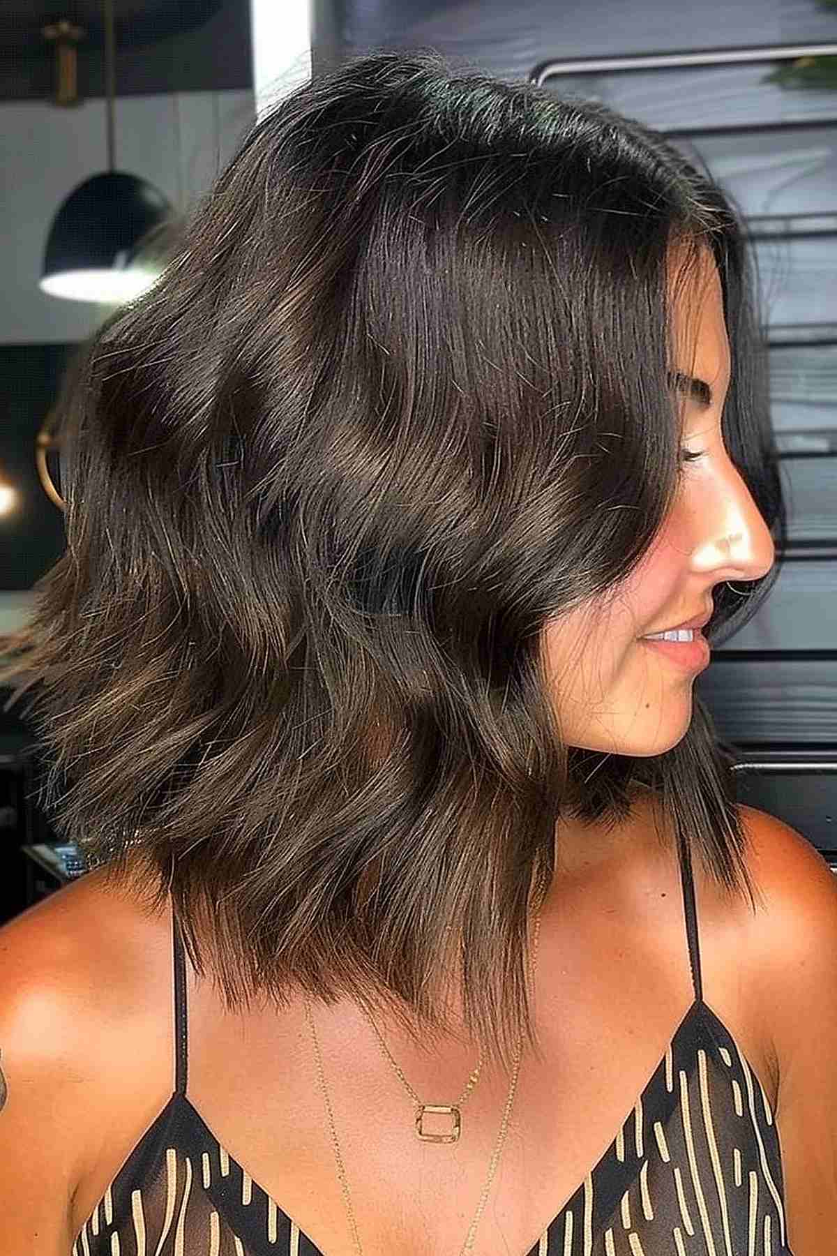 Side view of a woman with a long choppy inverted bob in deep brown
