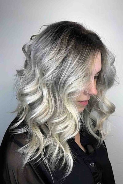 A Long ombre hairstyle transitioning from dark roots to smoky grey and ending in luscious platinum blonde curls