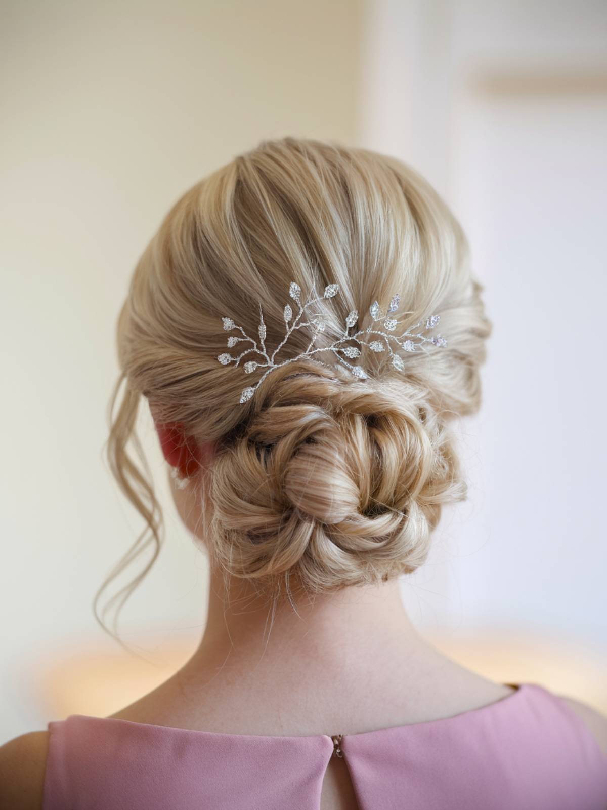 Elegant twisted low bun with soft face-framing tendrils and a delicate hairpiece for a romantic glam updo