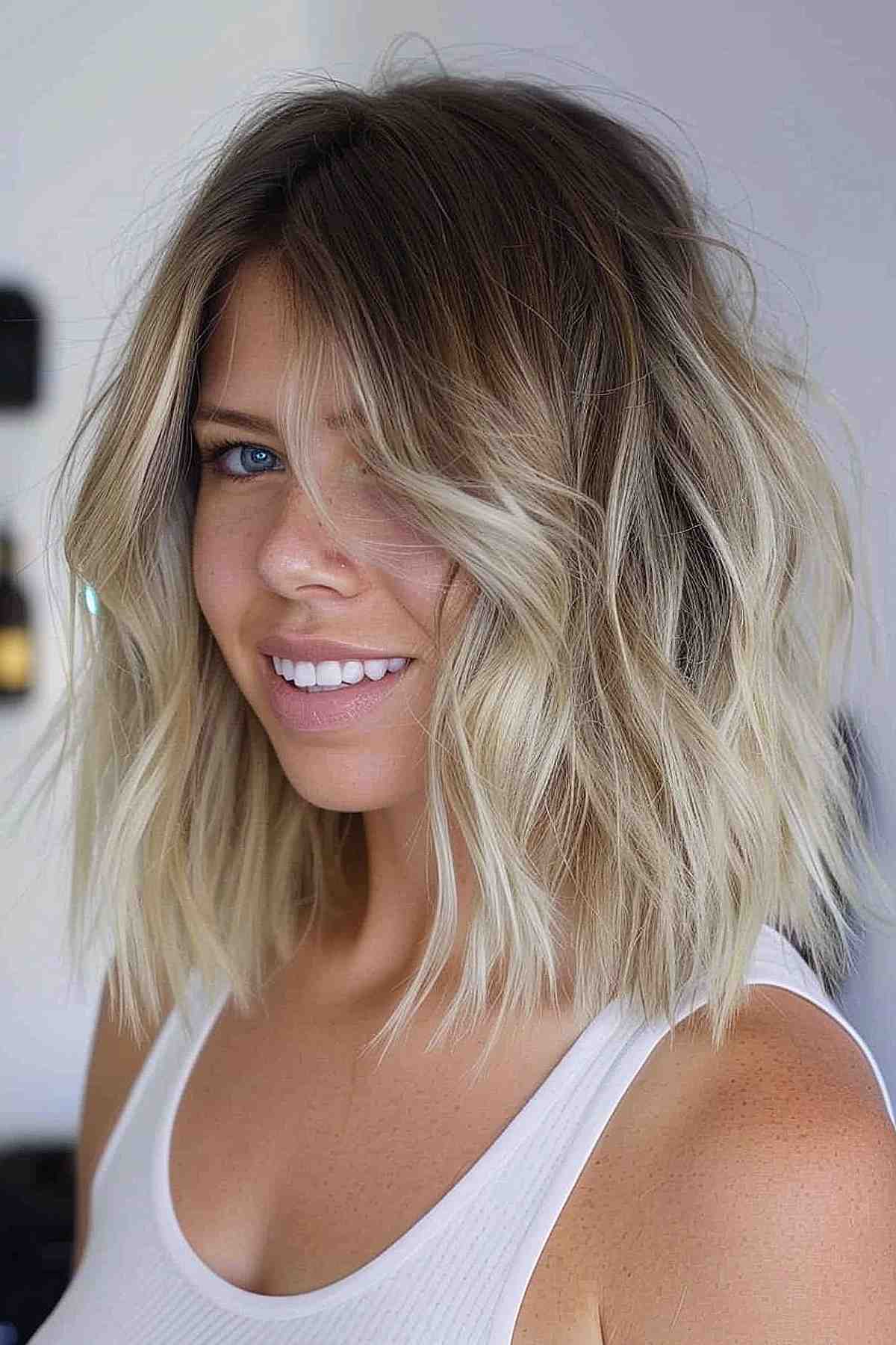 Long layered choppy bob with beachy waves and balayage from dark roots to platinum blonde tips.