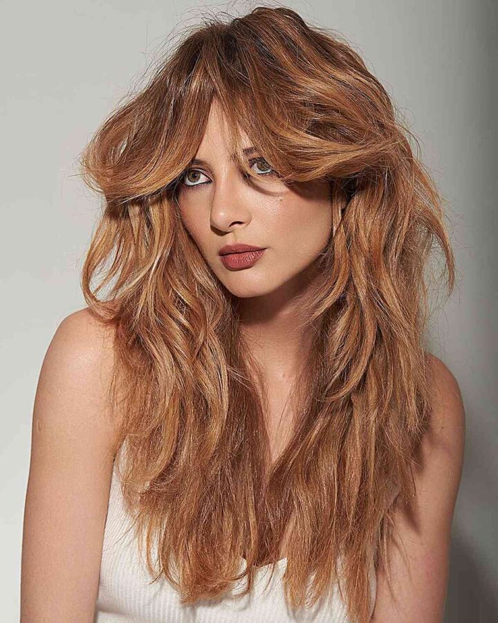 Long thick shaggy cut with curtain fringe and loose waves, offering a thick modern look