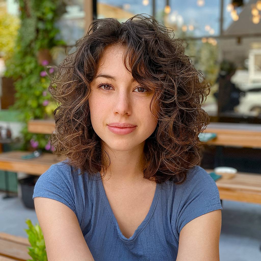 Shoulder-length curly hair with feathered fringe and soft layering for a relaxed curly style