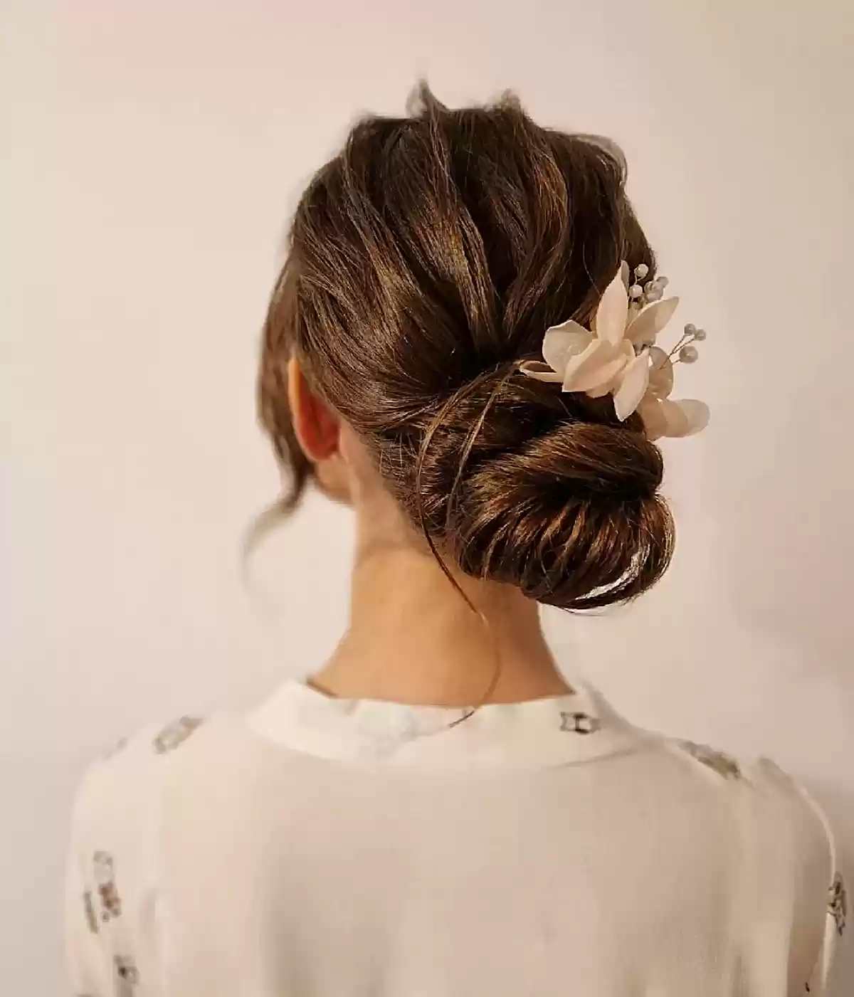 Low Pinned Bun for Long Hair with Pulled Strands and Flower Hair Accessory for Prom