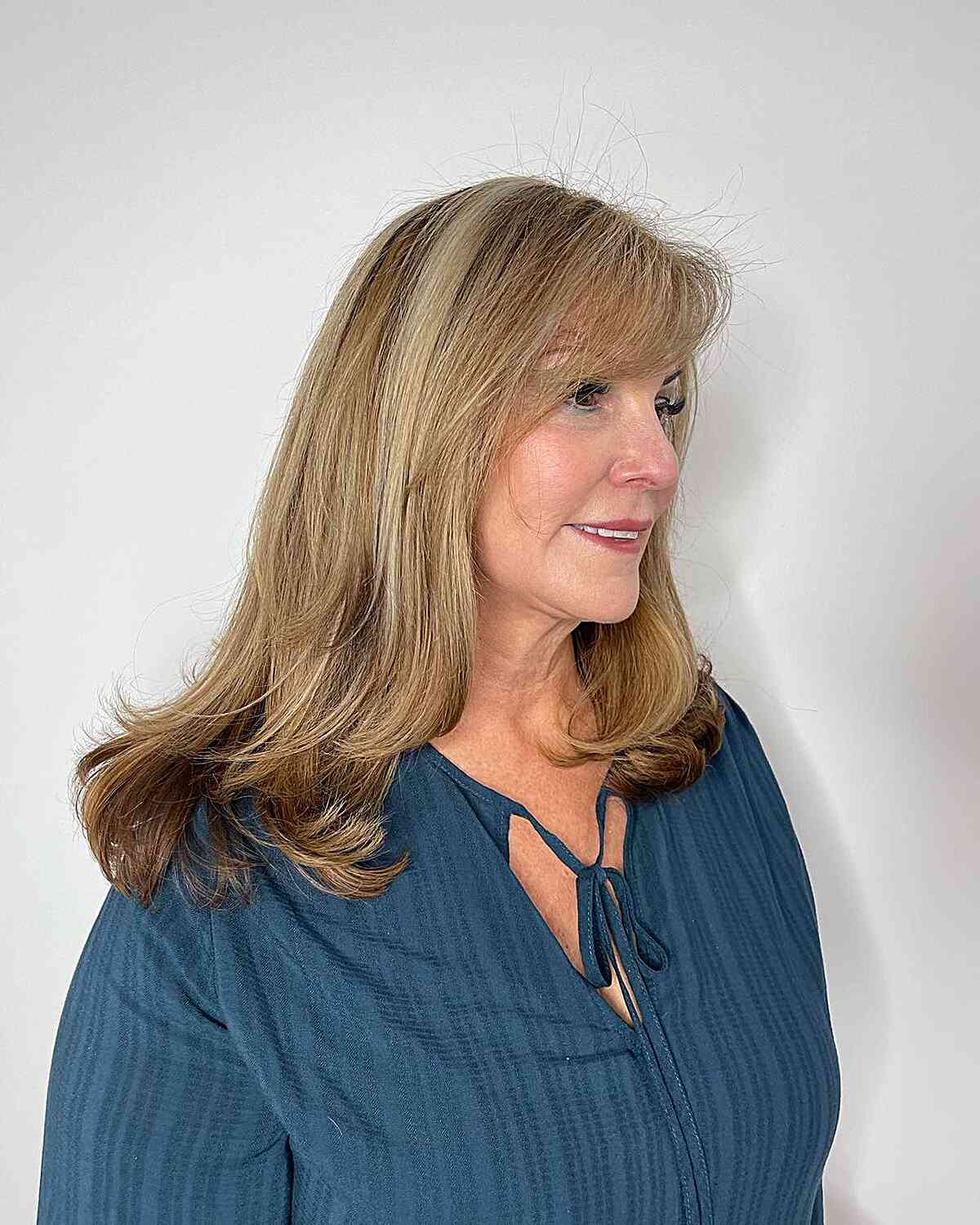Medium-Length Blowout Hairstyle with Face-Framing Layers and Side Bangs on Women Over 50