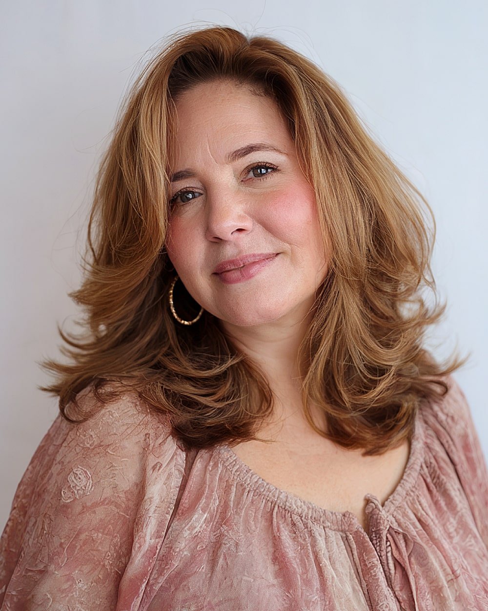 Layered medium haircut with flicked ends and golden brown color for round-faced women over 40