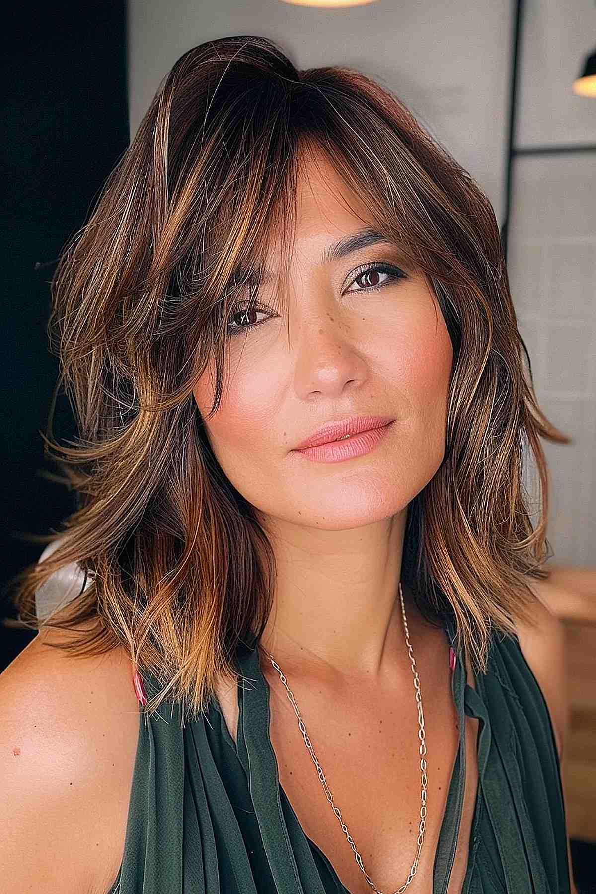 Shoulder-length layered hairstyle featuring side-swept bangs and warm brown highlights specifically designed for square faces