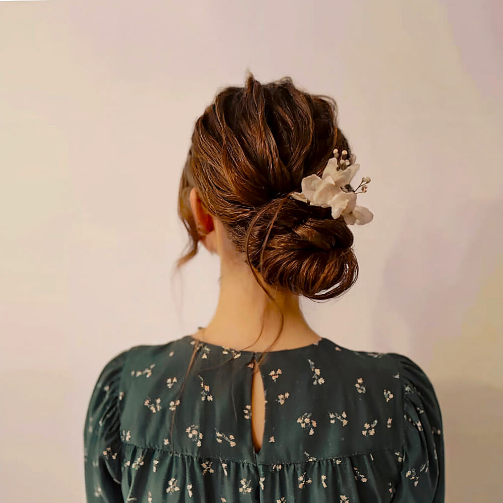 Elegant Low Pinned Bun with Pulled Strands and Floral Hair Accessory for Prom