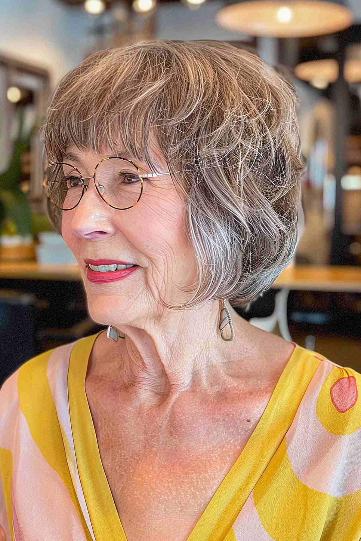 Textured bob with bangs for older women with glasses, showcasing soft, wispy layers and a youthful, face-framing cut.