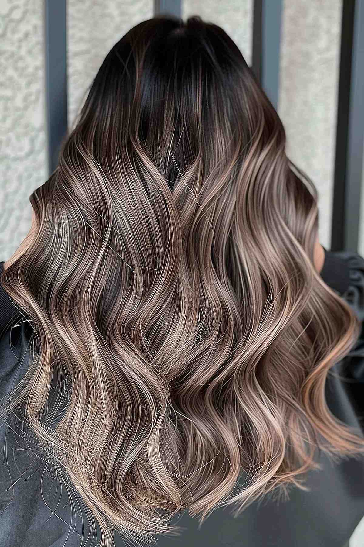 Luxurious long waves in mushroom brown with dark roots, featuring a balayage technique that enhances the hair's natural volume and depth.