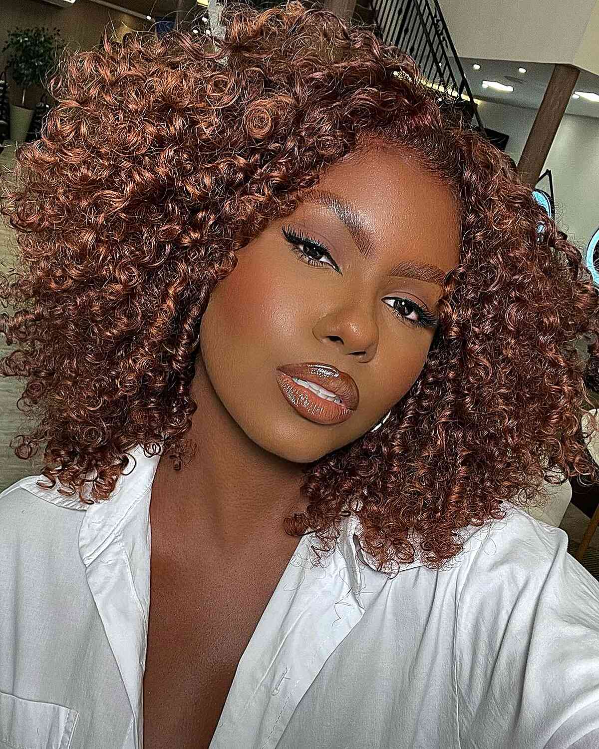 Natural curls in a middle-parted Cadō cut with a warm auburn color, offering volume and defined ringlets for a balanced look.